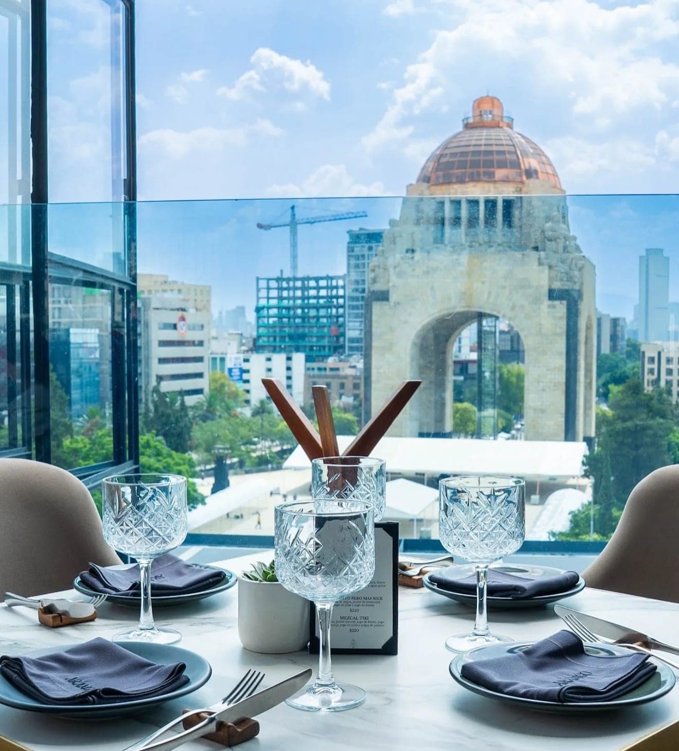 A table set with cut-crystal glassware in front of a window framing the Monumento a la Revolución