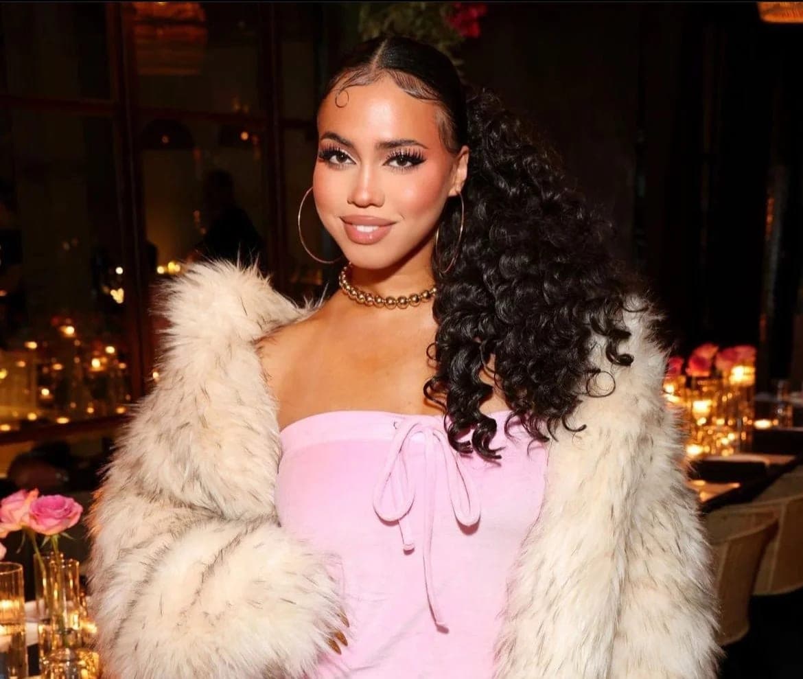 A guest in a pink dress and cream fur coat at a candlelit dinner in the dining room