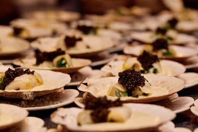 Rows of scallop shells topped with caviar, lined up for service.