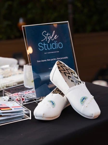 A pair of white TOMS slip-ons displayed beside a Style Studio sign.