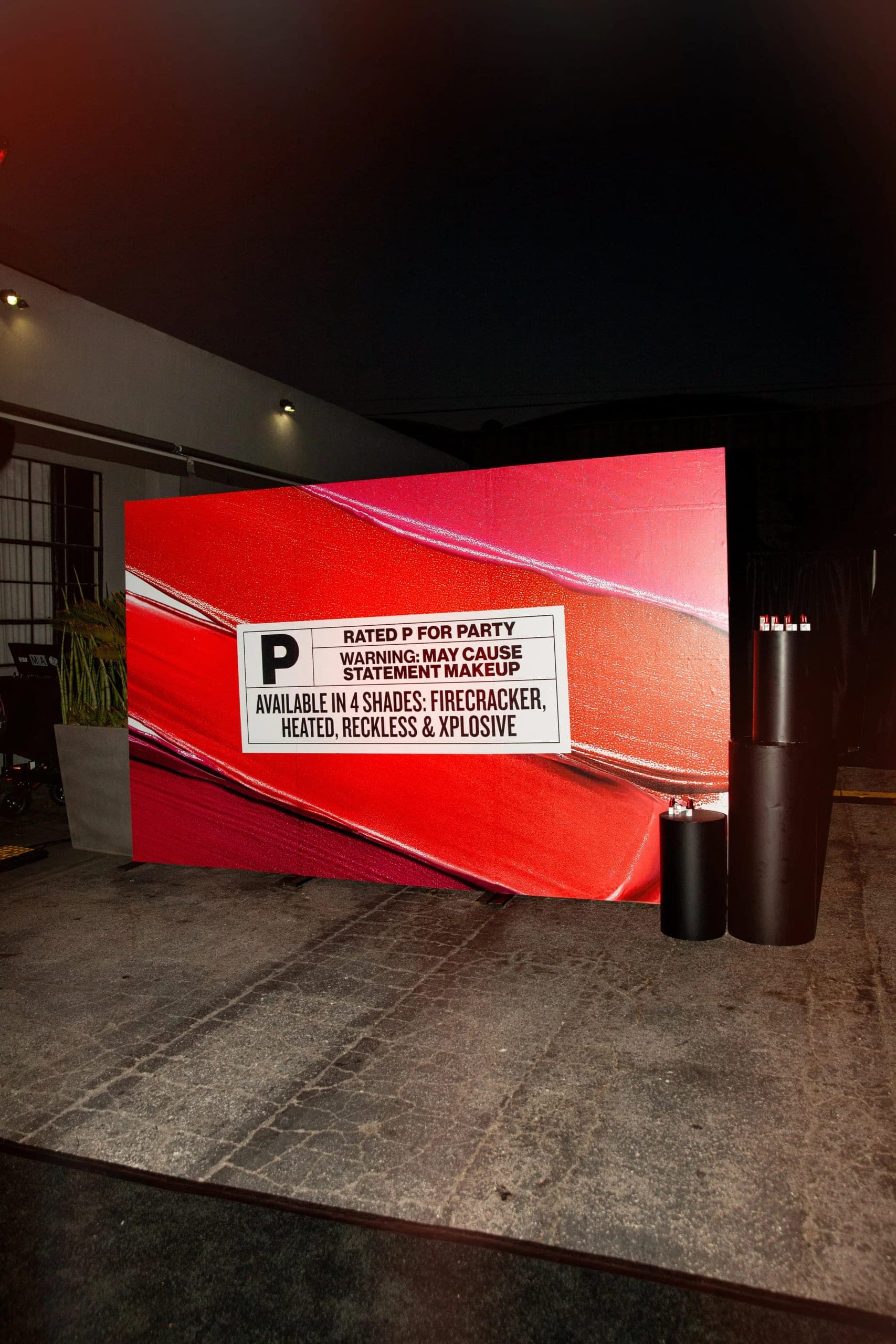 A large red brand billboard installed against a warehouse wall at night