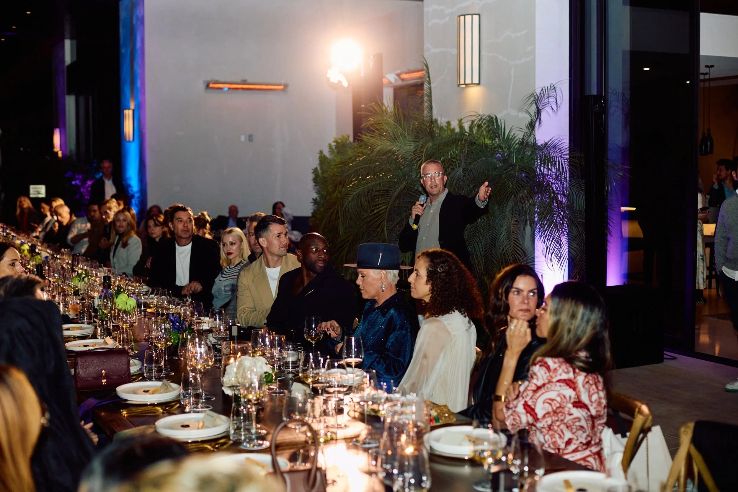 Guests seated the length of the dinner table listening as a host speaks