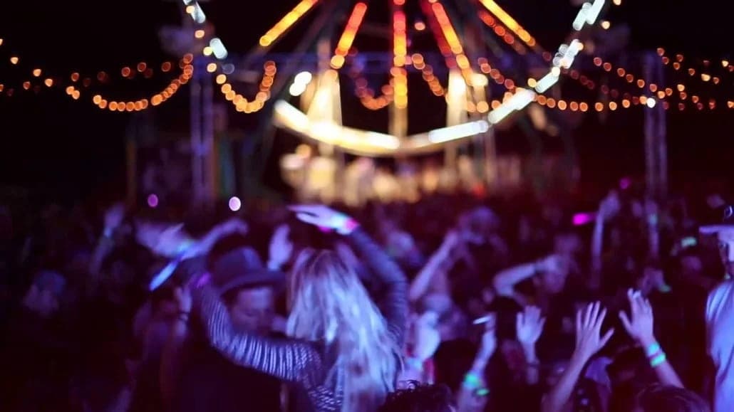 Dancers with their hands in the air beneath the spinning lights of a carnival swing ride