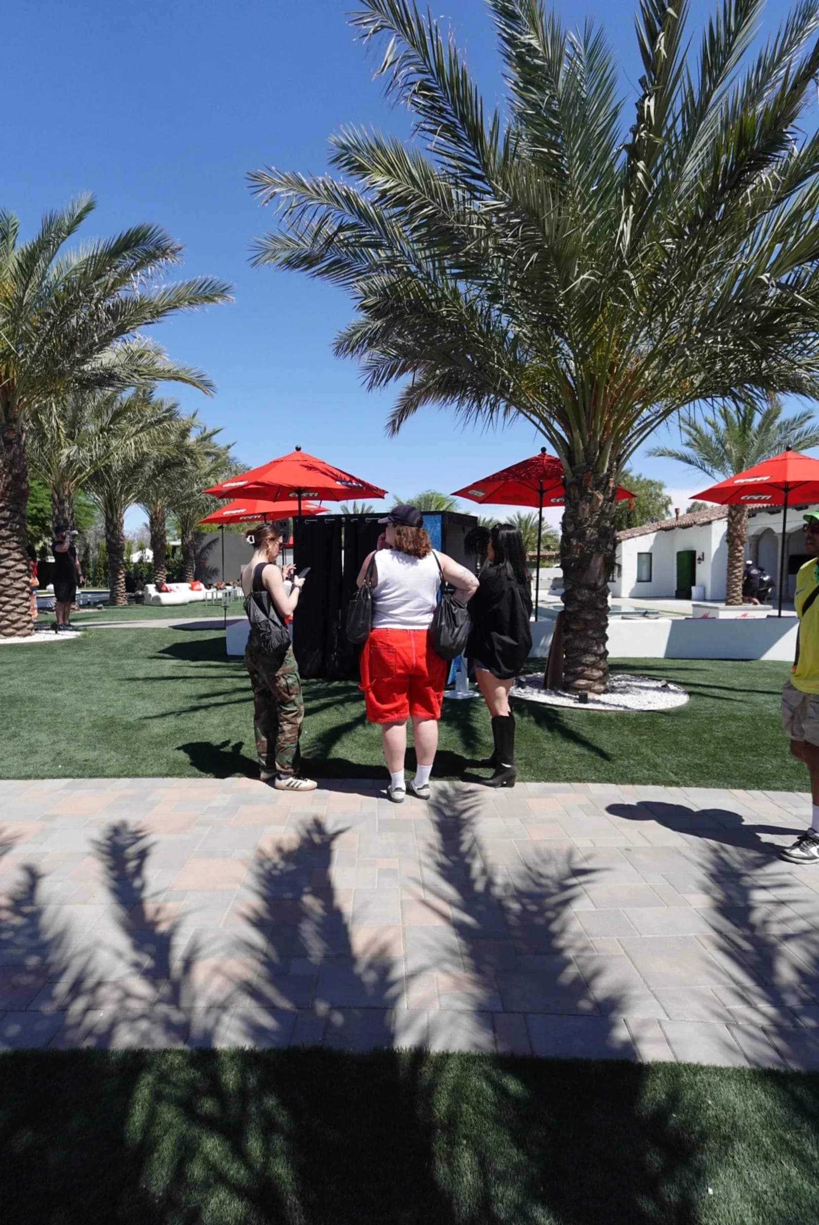 Guests crossing the lawn between date palms and red Cacti umbrellas in the desert afternoon