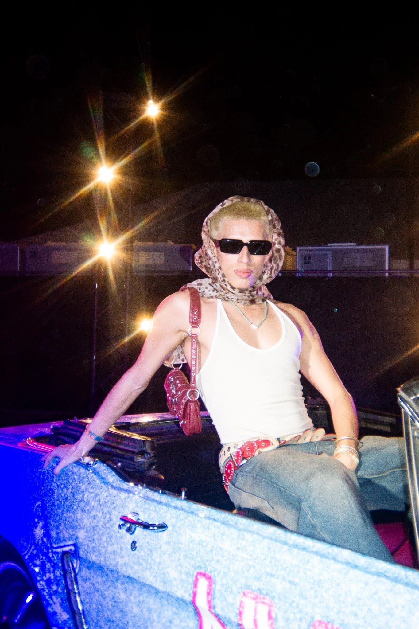 A guest sitting on the tailgate of a lit pickup at Neon Carnival, starbursts of light behind