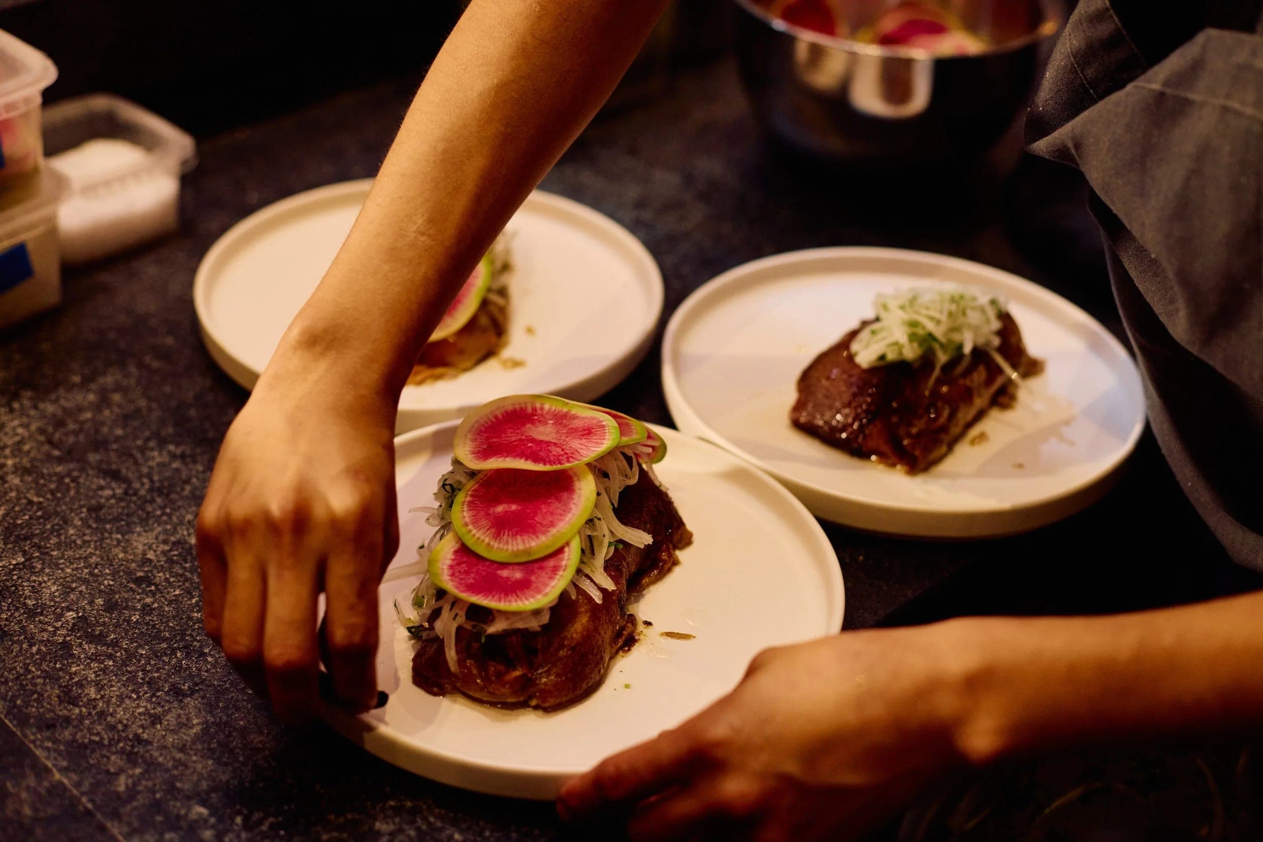 A server's hands setting two plates of seared tuna down on the table during dinner service