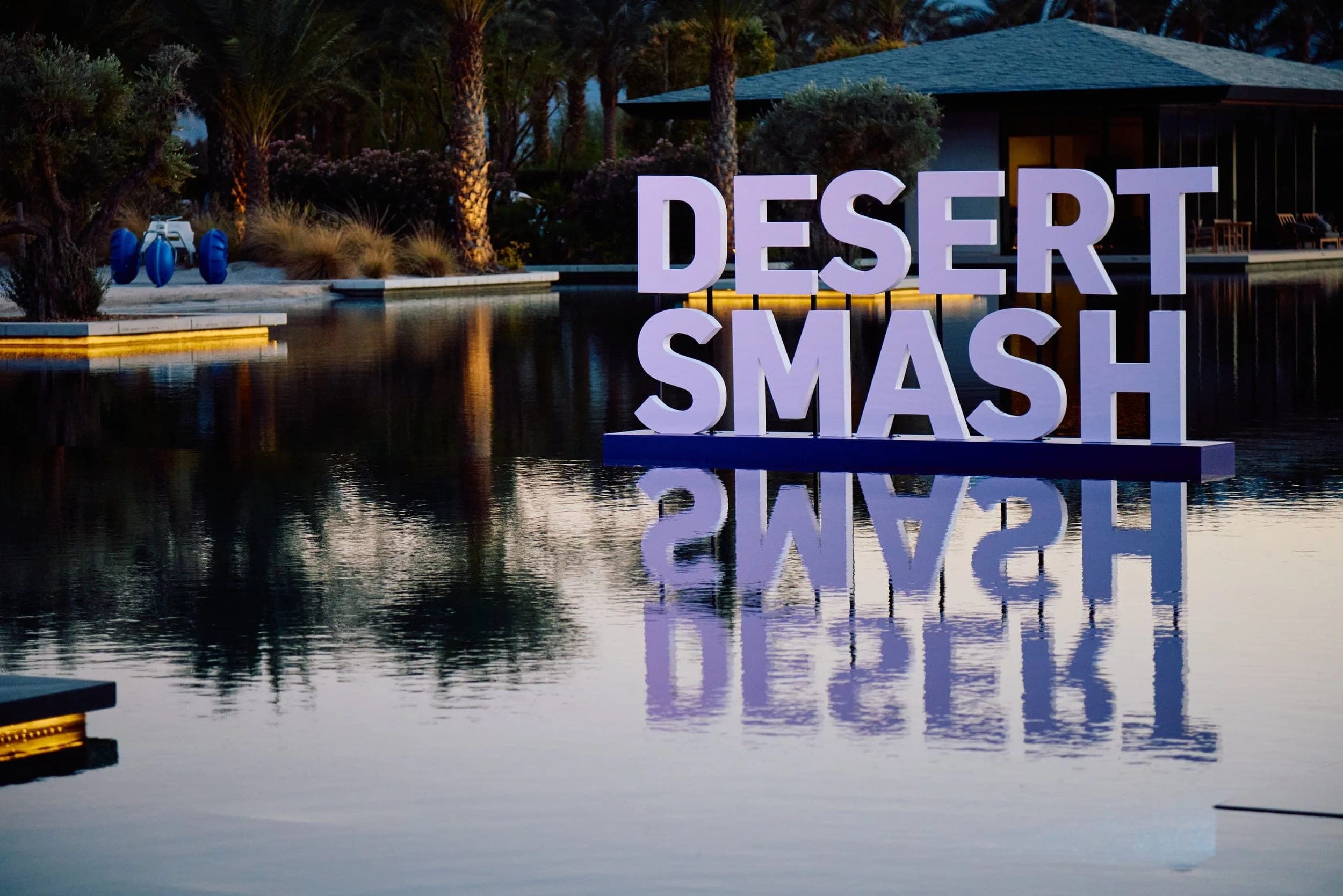 The Desert Smash sign standing at the edge of the reflecting pool at Zenyara Estate, its letters mirrored in still water at dusk