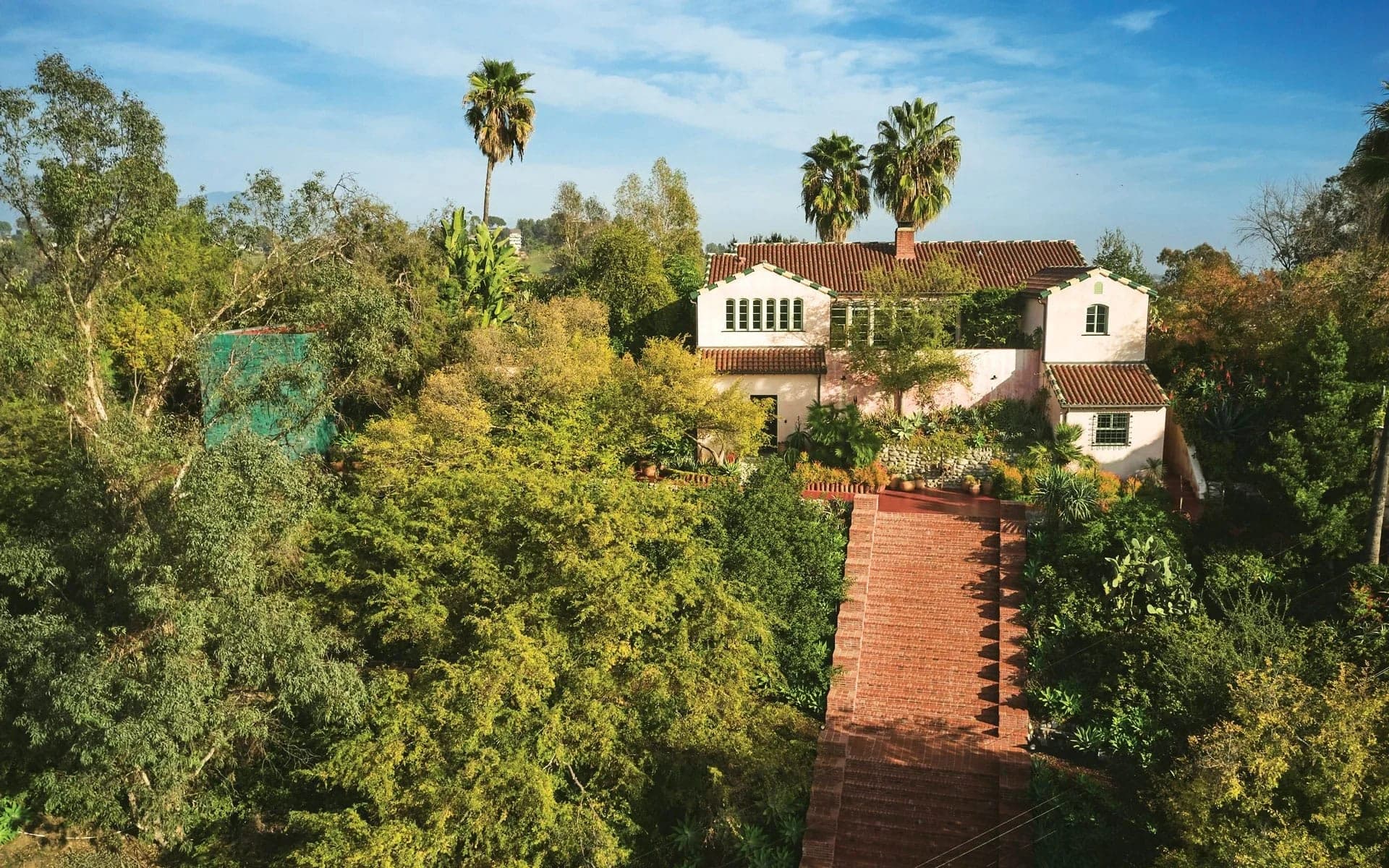 The Flamingo Estate house seen from above, a brick path climbing through dense subtropical planting