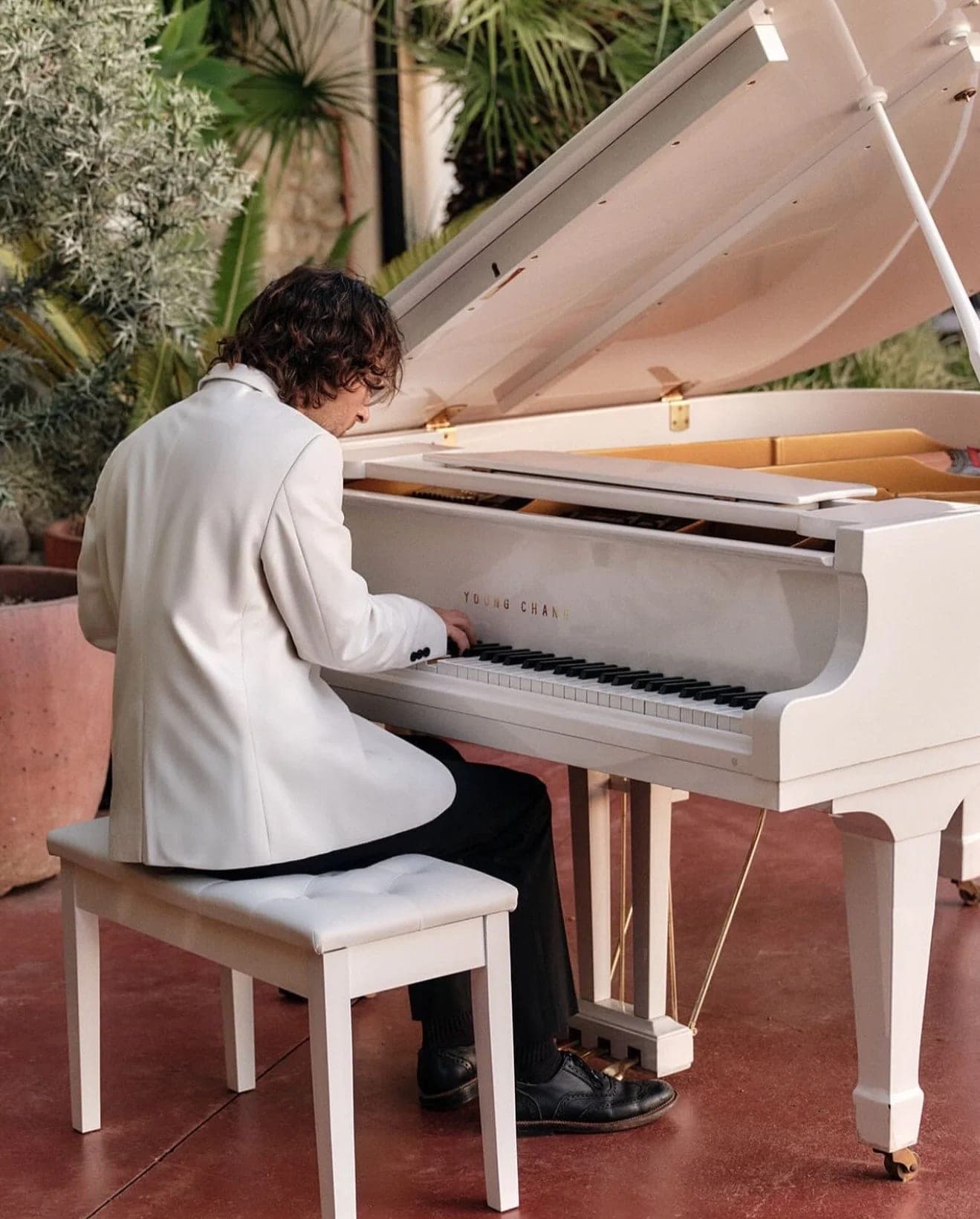 A pianist in a white jacket playing an open white grand piano on the terrace