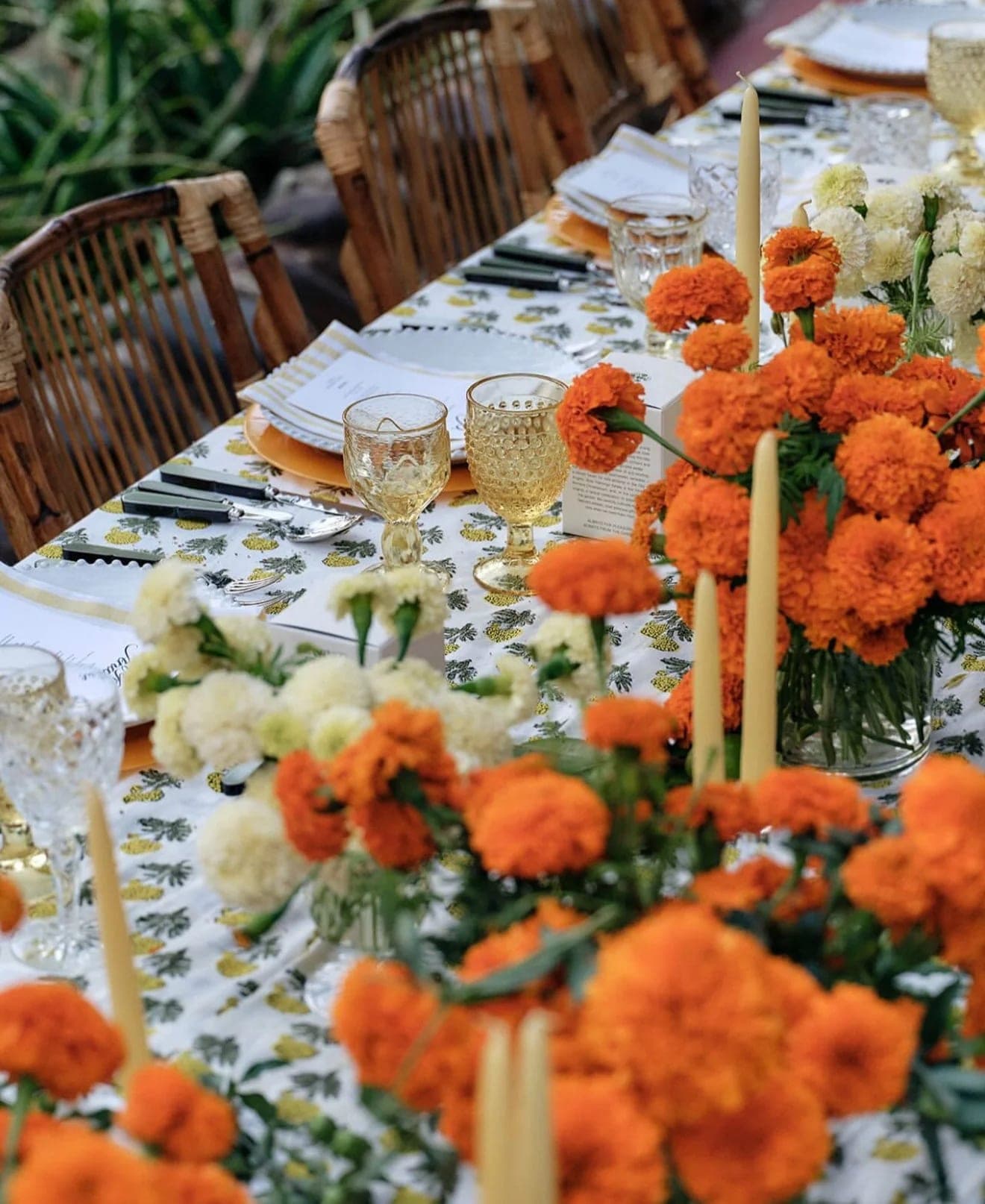 Close view of the tablescape: marigold and white blooms crowded between cream tapers and etched glassware