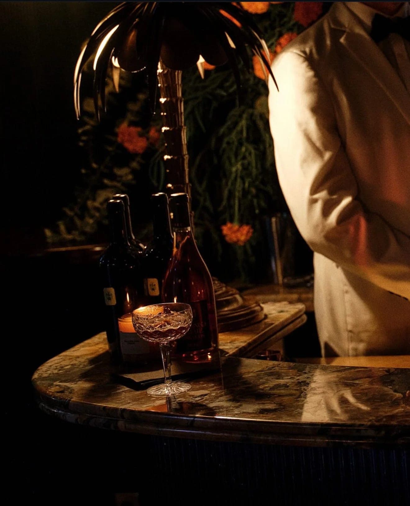 Wine bottles and a lit candle on a dark marble side table, a server standing just beyond