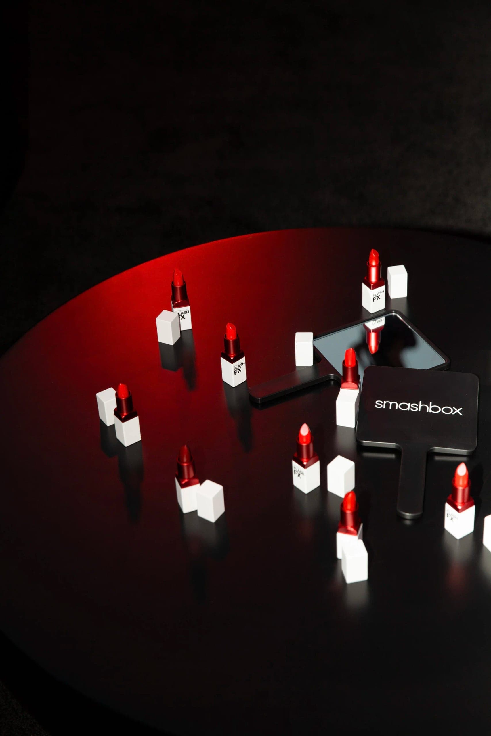 Lipsticks and their boxes arranged across a black plinth under a single red spotlight