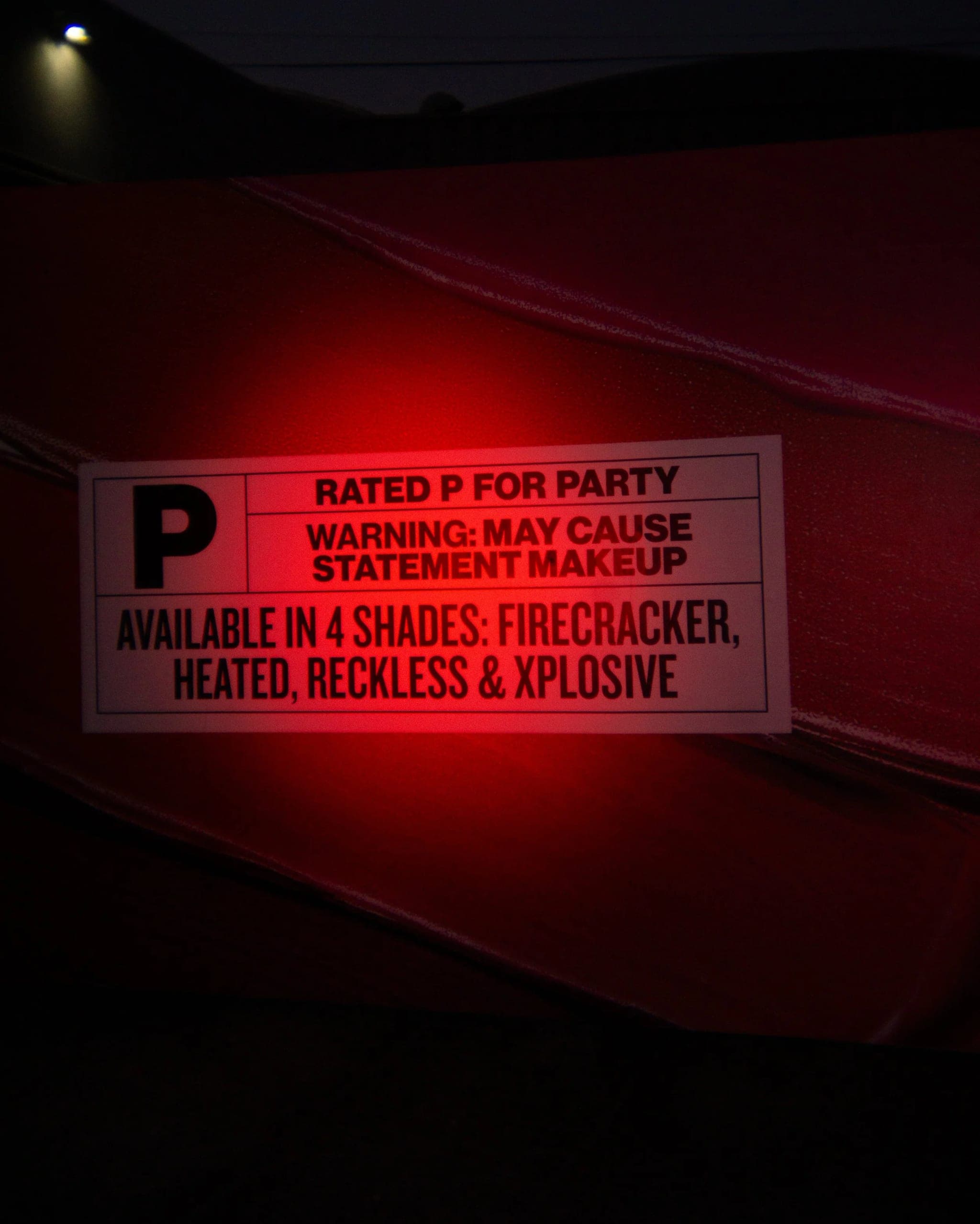 A 'Rated P for Party' warning placard mounted on a red-lit wall, listing the four lipstick shades