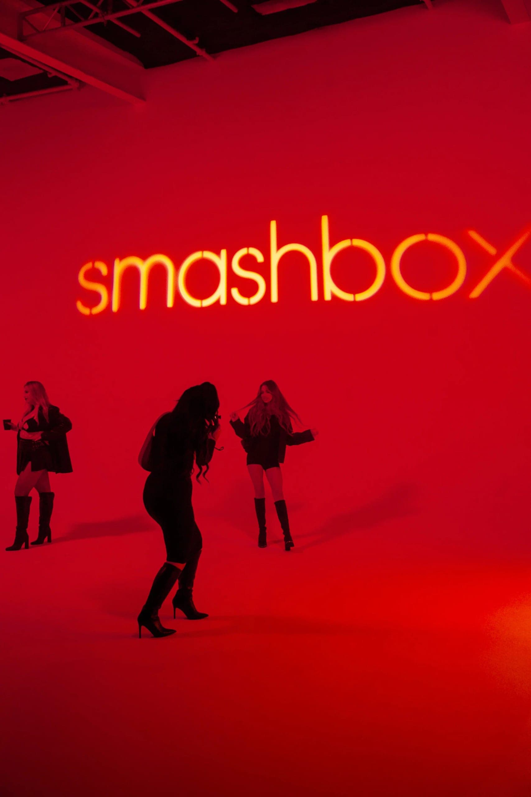 Three guests silhouetted against a saturated red wall lit with the Smashbox wordmark