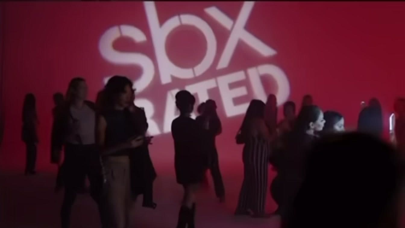 The SBX Rated launch for Smashbox Cosmetics — guests moving through the room, washed red against the projected sign.