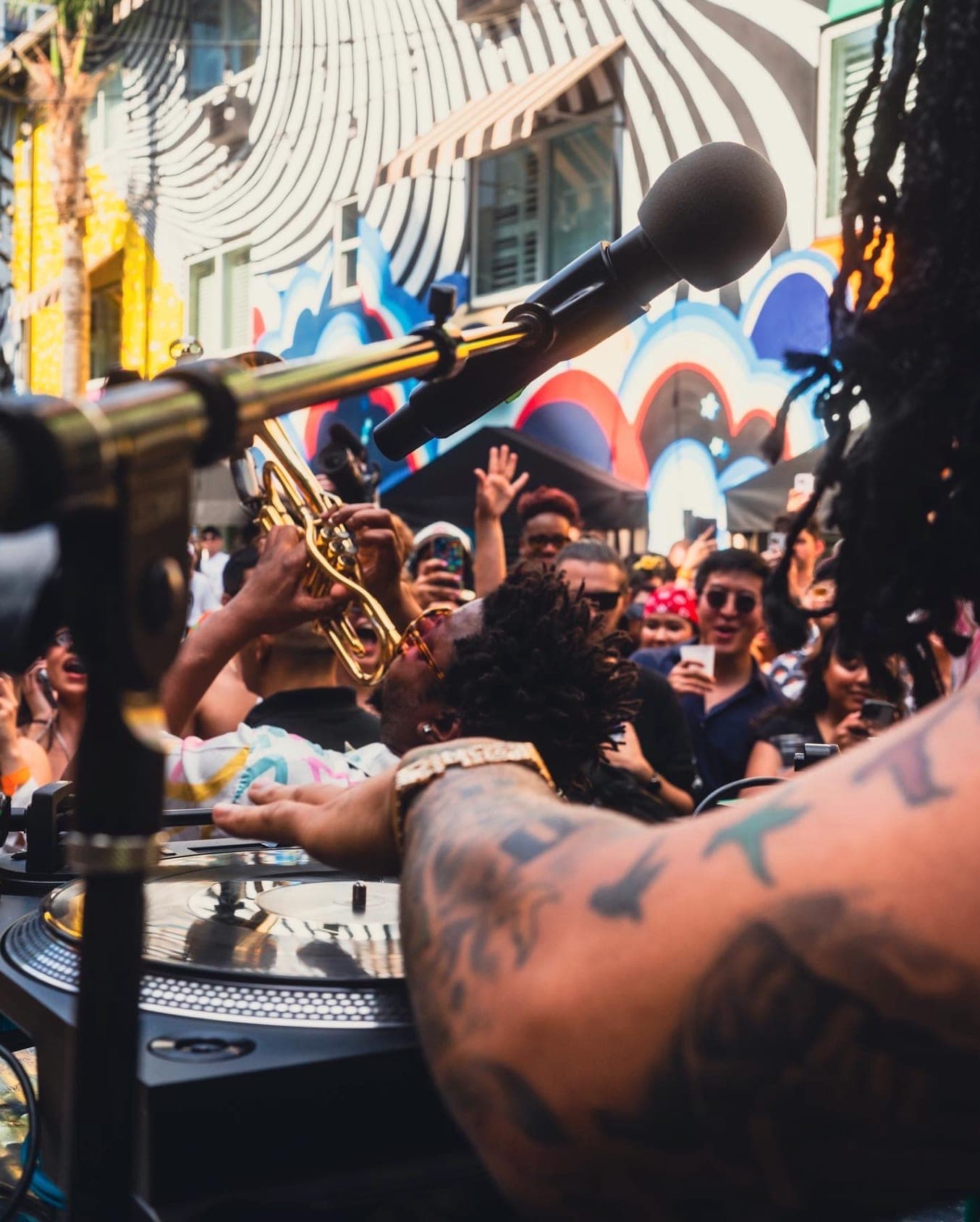 A trumpet raised over the turntables as the crowd's hands go up behind it