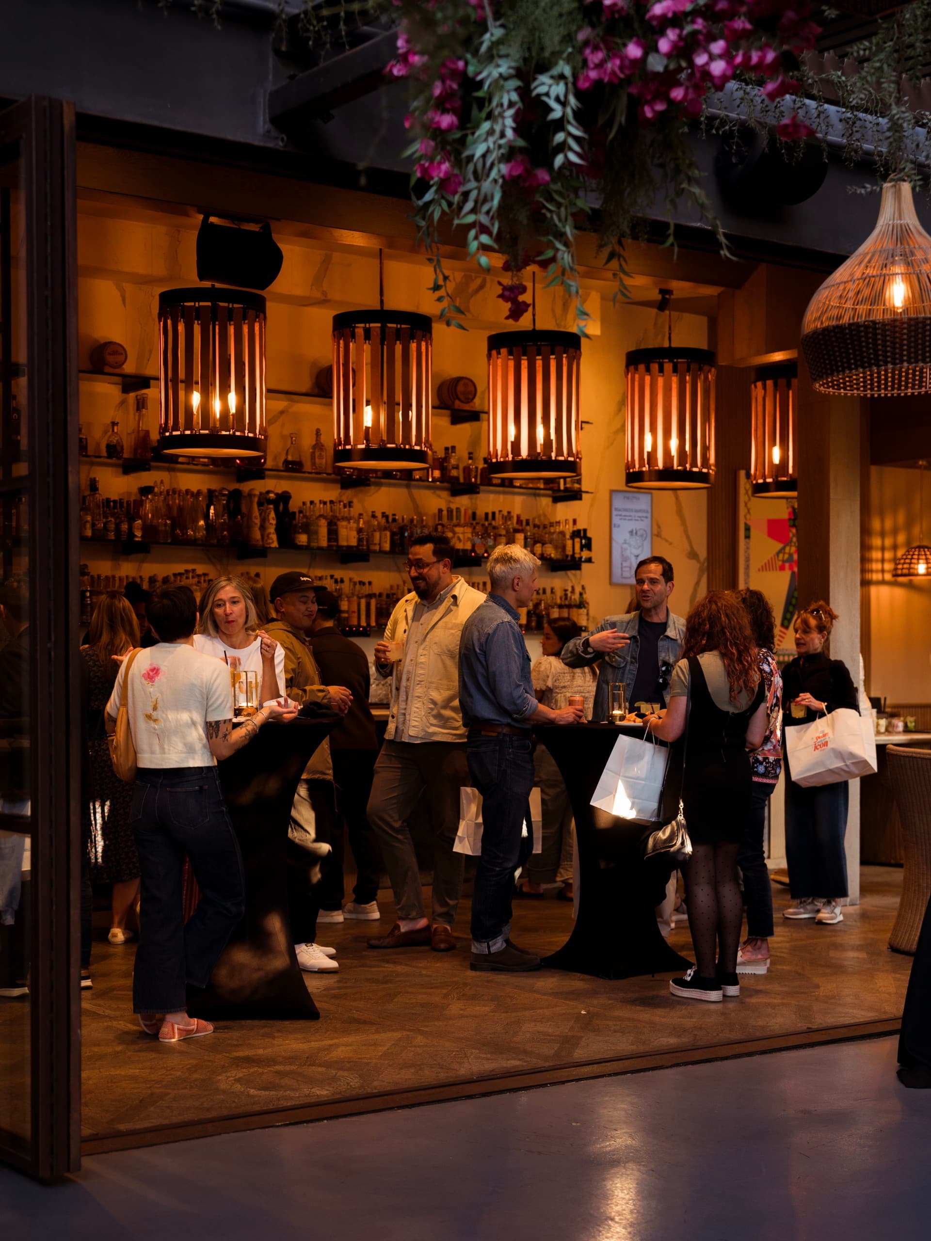 Guests talking over drinks in Paloma’s indoor bar, under a row of pierced brass lanterns and a canopy of orchids.