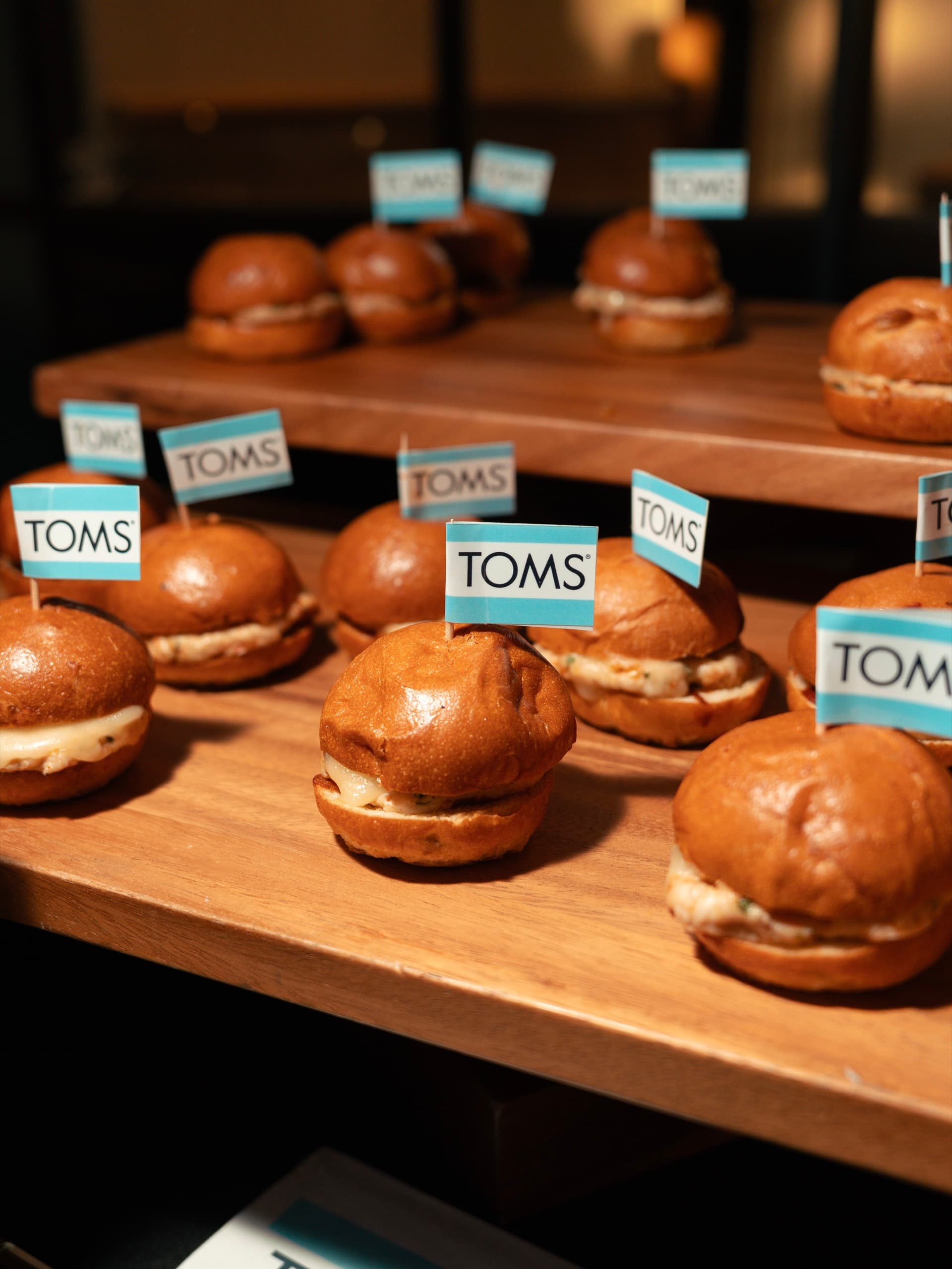 Tiered wooden boards of brioche sliders, each one flagged with a small TOMS card.